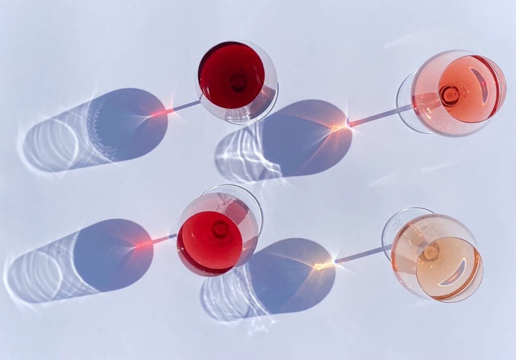 Four wine glasses filled with diverse shades of rosé wine on a light blue background