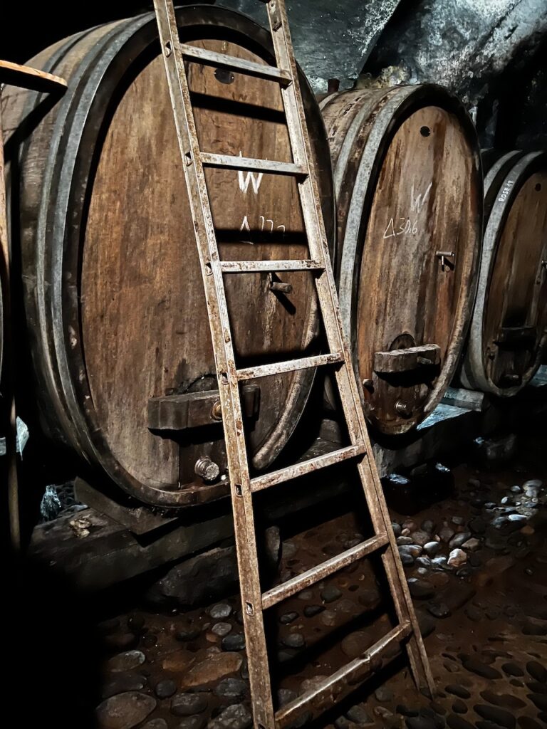 Wooden ladder leaning against doppelstück, chalk marked winebarrels in an underground cellar with a stone floor