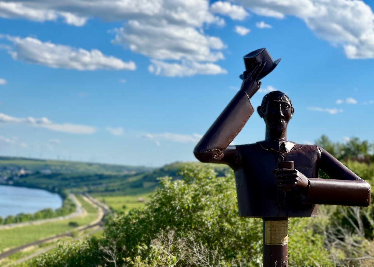 Bronze statue tipping his hat above a German Riesling vineyard on Rheinhessen's Roter Hang