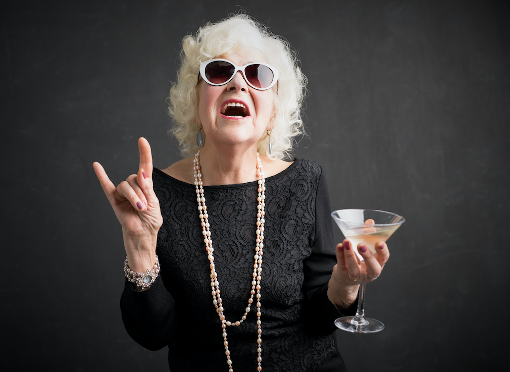 Old woman in sunglasses, a black dress and pearls holding a martini glass