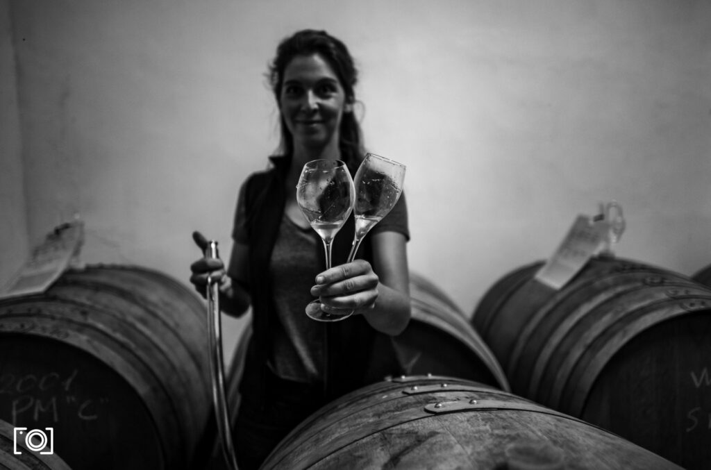 Sparkling wine producer Marie Raumland holding a glass of sekt in front of winebarrels