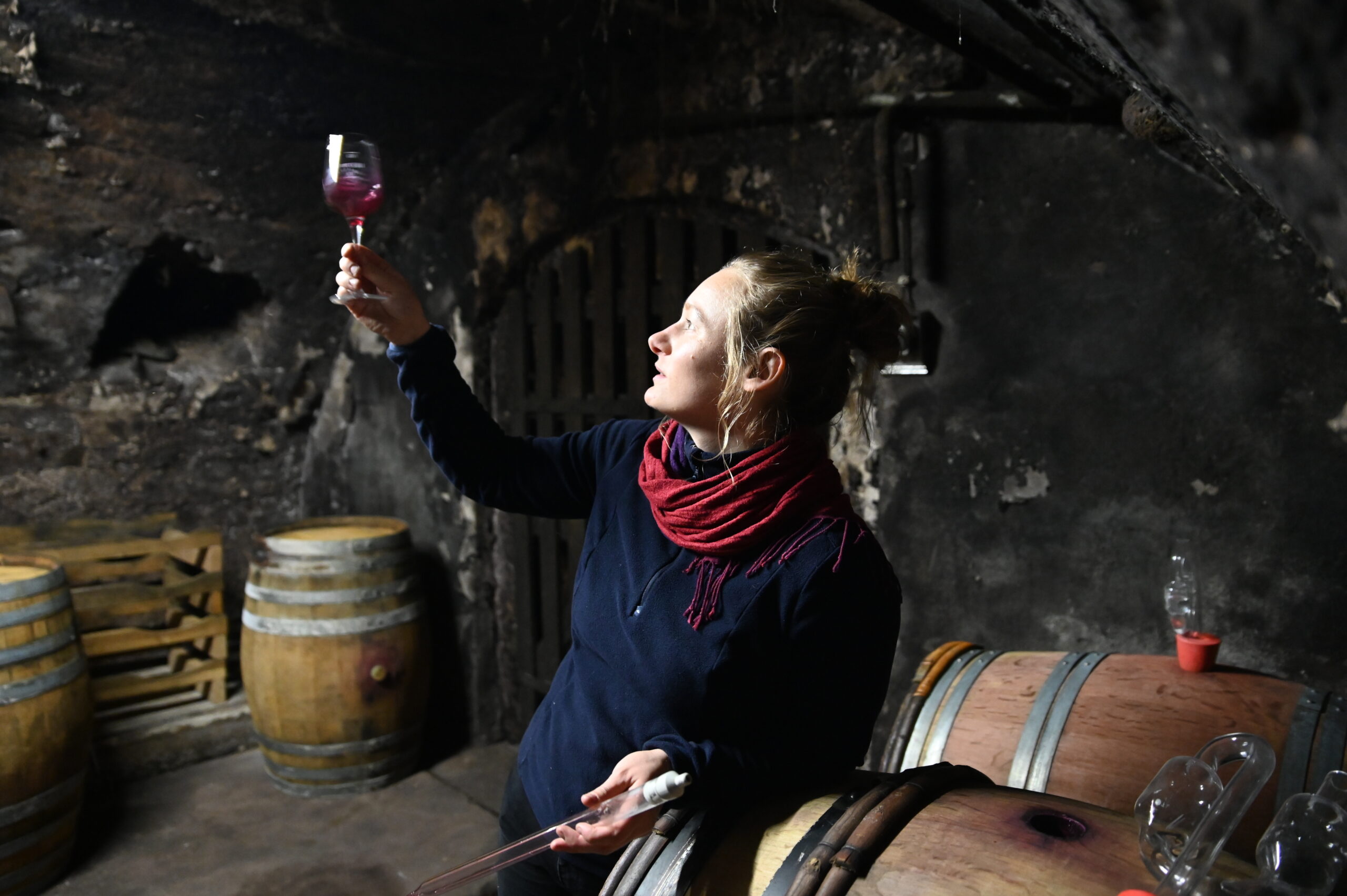 Winemaker Christine Pieroth in cellar inspecting a raised glass of red wine in the light