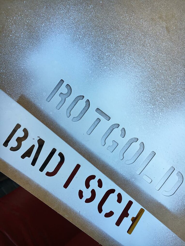 Stenciled lettering on a white metallic background spells out ROTGOLD and BADISCH