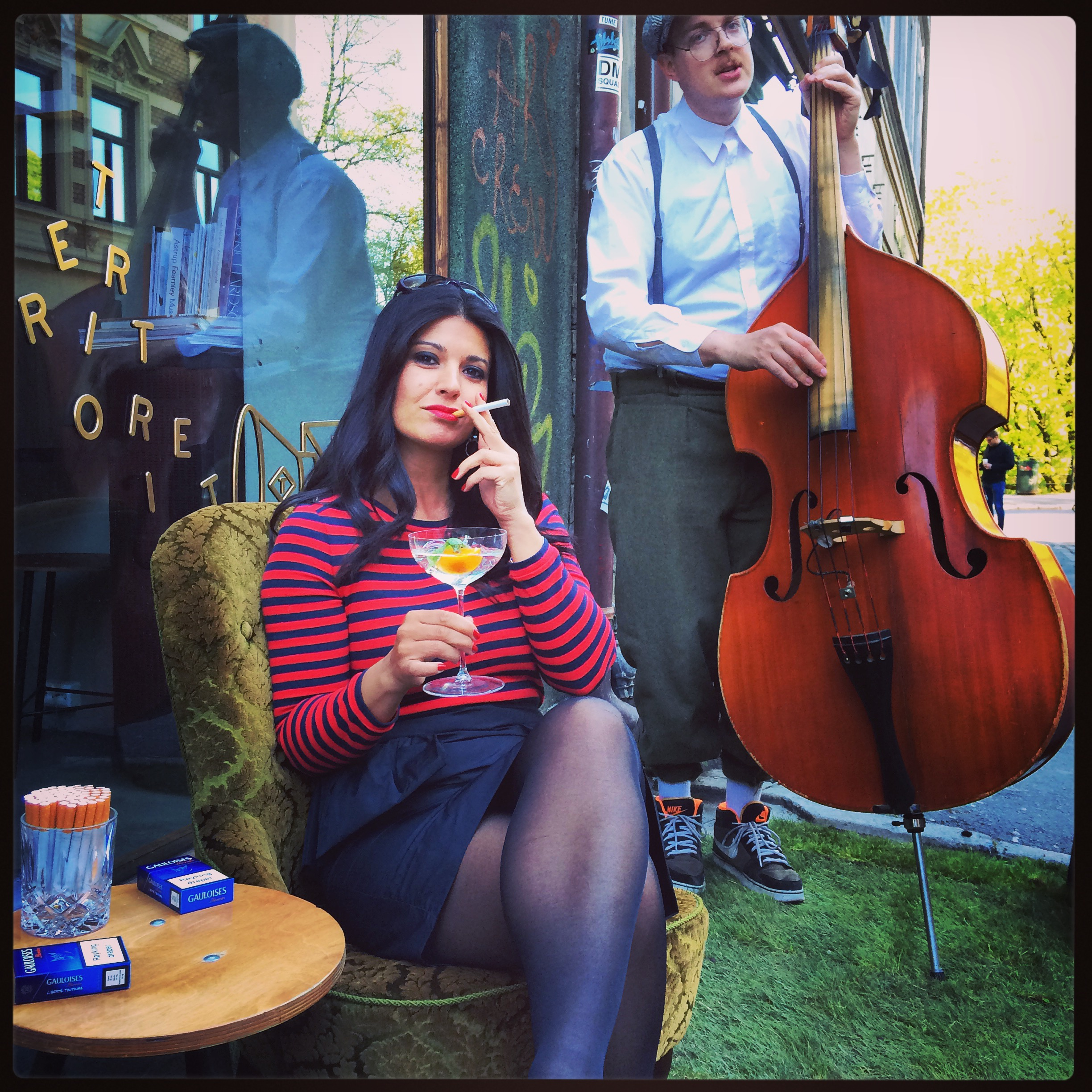 Woman posed stylishly on velvet chair smoking and drinking a martini. Cello player in background.