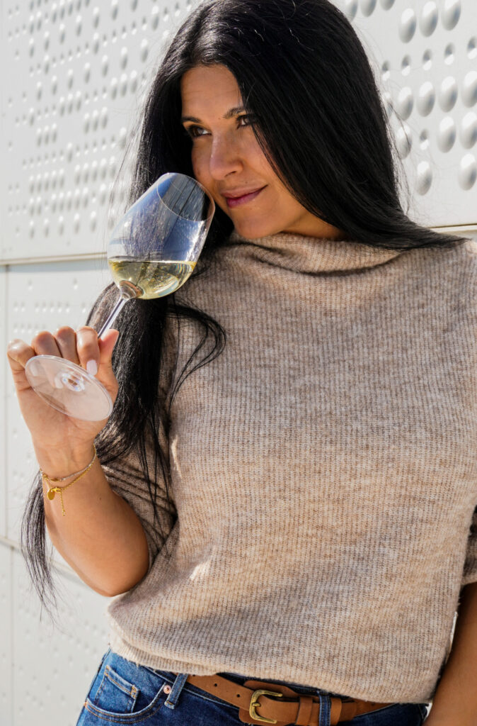 Woman smelling white wine glass and leaning against a white textured wall
