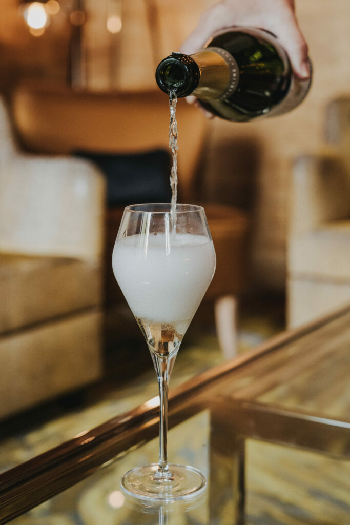 Champagne being poured into a stylized wine glass on a glass table