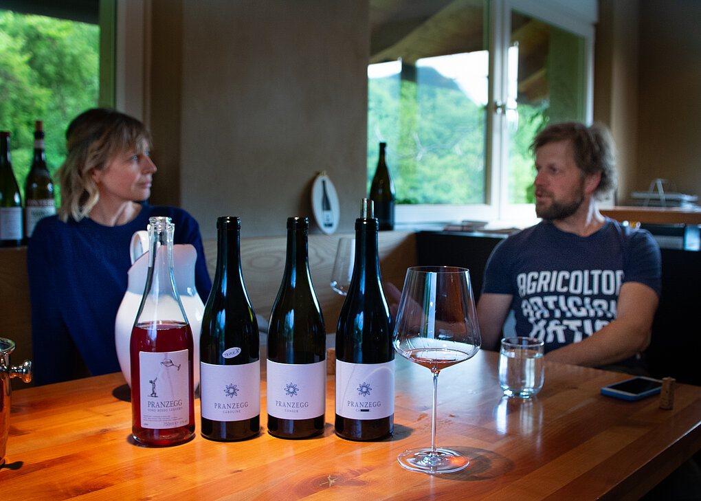 Man and woman sitting at a wooden table with 4 bottles of Pranzegg wine and one glass.