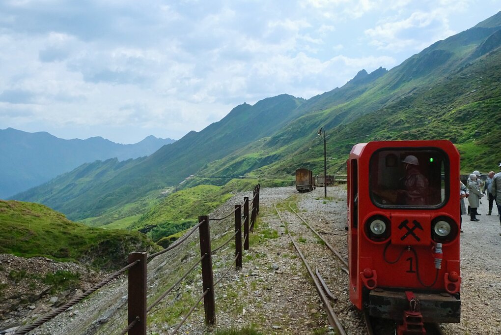 Red mining car on tracks in Alto Adige. Grass covered mountains in background