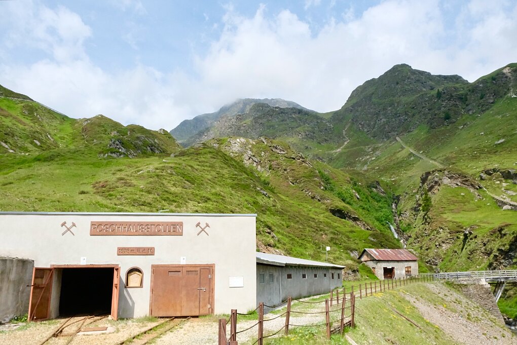 Clay colored mining building with open doors and grass covered mountains in background