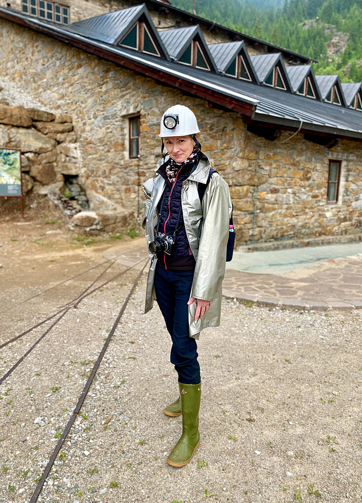 Woman stands in mining hat and boots in front of Alto Adige mine where the Epokale wine is aged.