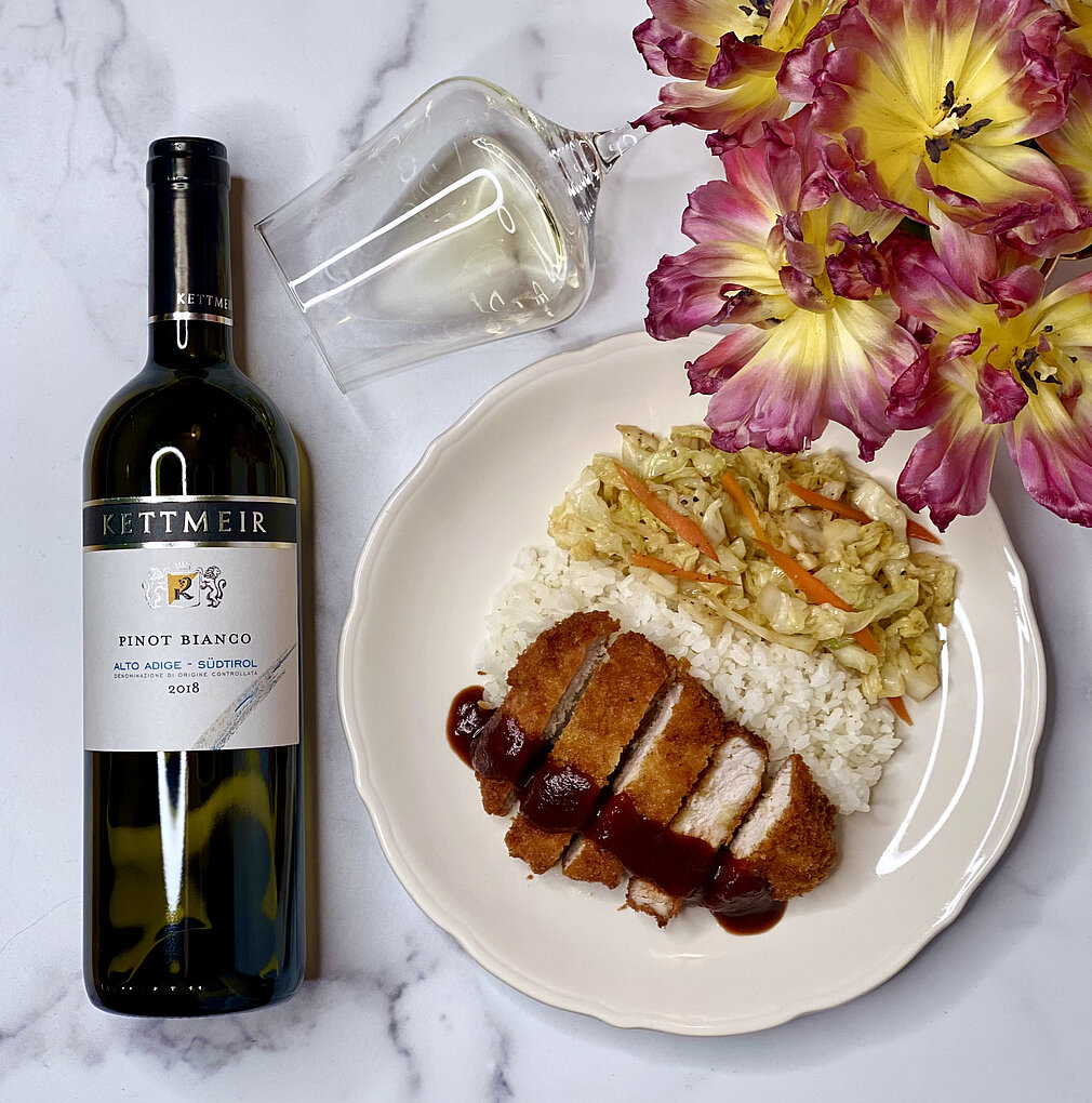 Bottle of Pinot Bianco from Kellmeir next to plate of Tonkatsu, rice and vegetables. Flower bouquet and horizontal wine glass