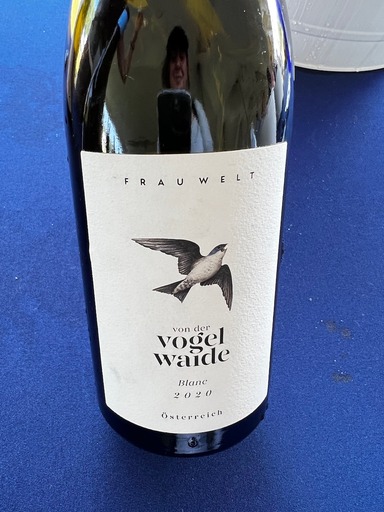 Royal blue background, with dark glass wine bottle in foreground. Large white label feautres drawn bird logo and words vogel waidee