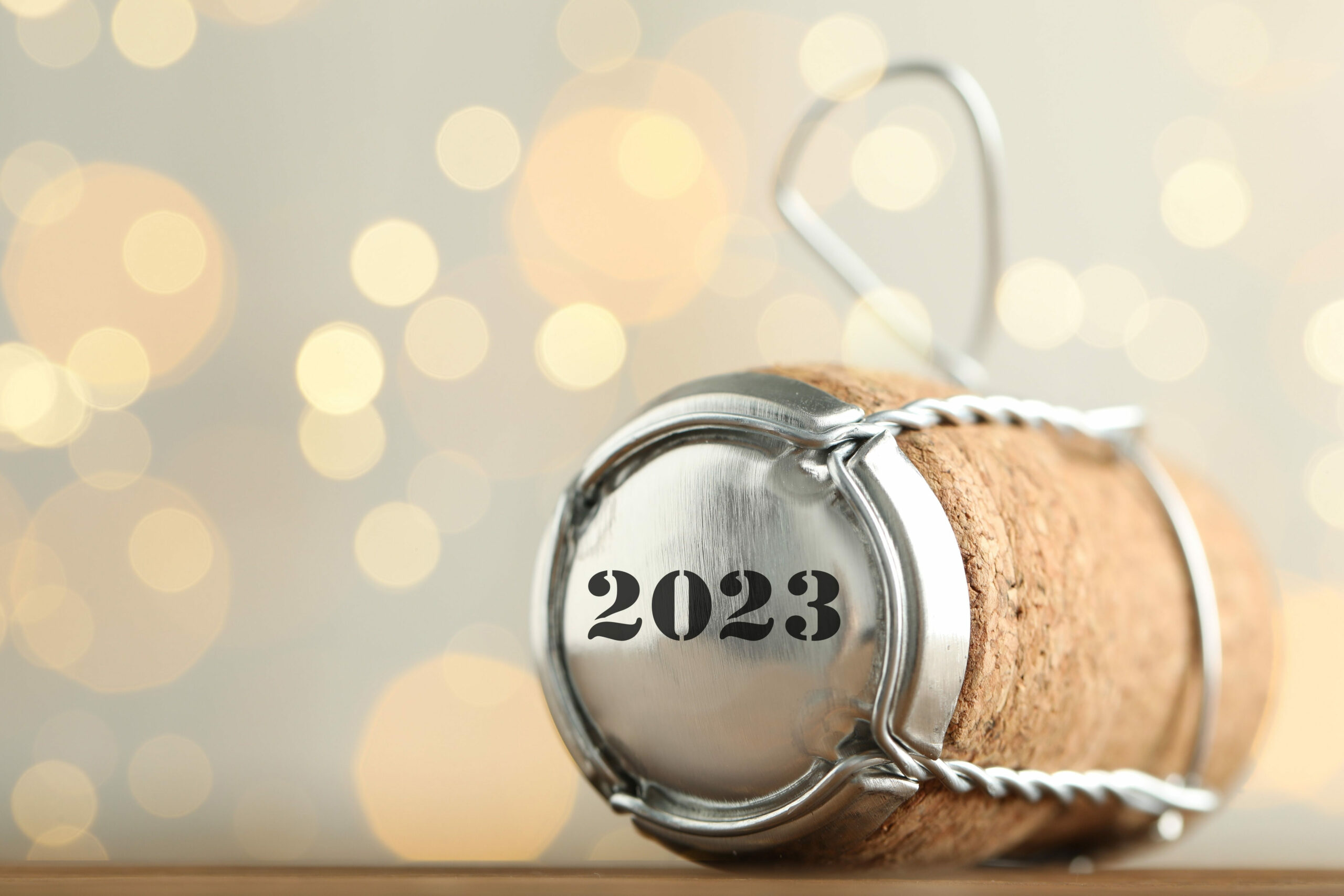 Sparkling wine cork and capsule with 2023 written on it against a sparkly silver and gold background.