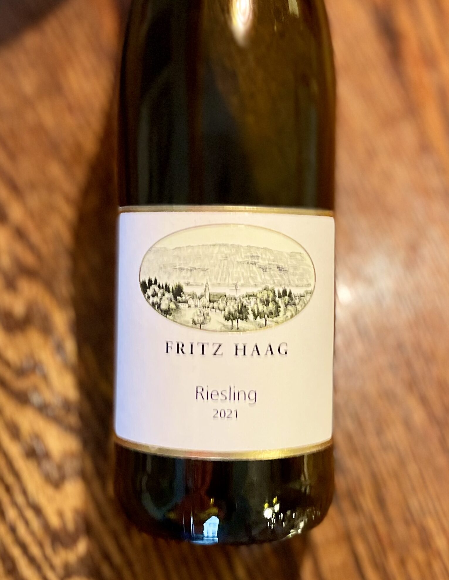 Brown glass wine bottle with small white label featuring drawn image of vineyards and the words FRITZ HAAG RIESLING 2021