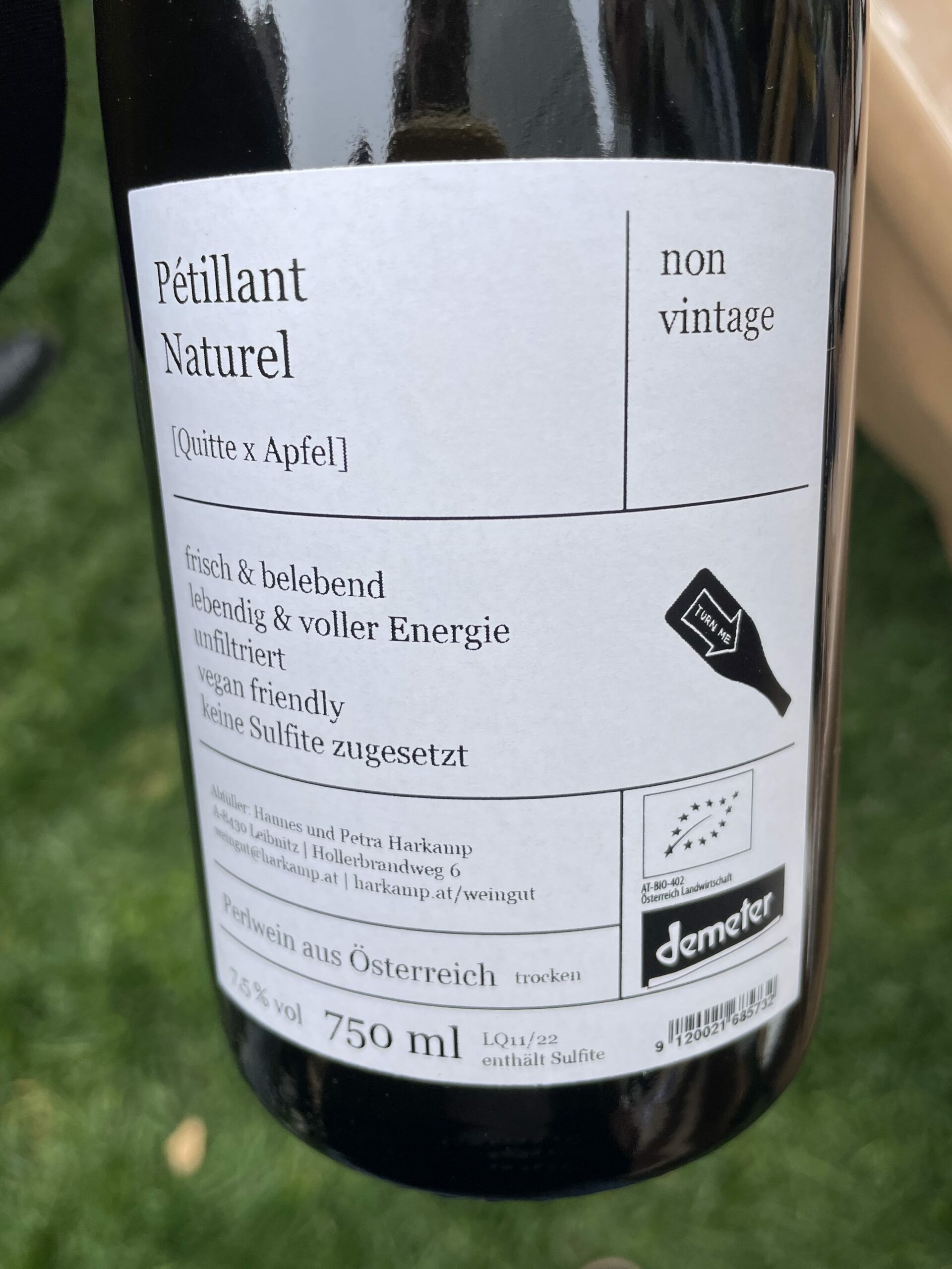 Against a grass background, a wine bottle with a large white label reads Petillant Naturel Quitte x Apfel non vintage. Includes logo for EU organic wine and demeter biodynamic certification.