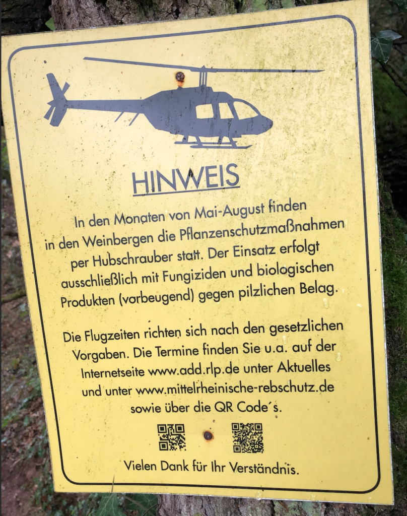 A sign in German warns of the use of helicpoters to spray synthethic materials during summer months.