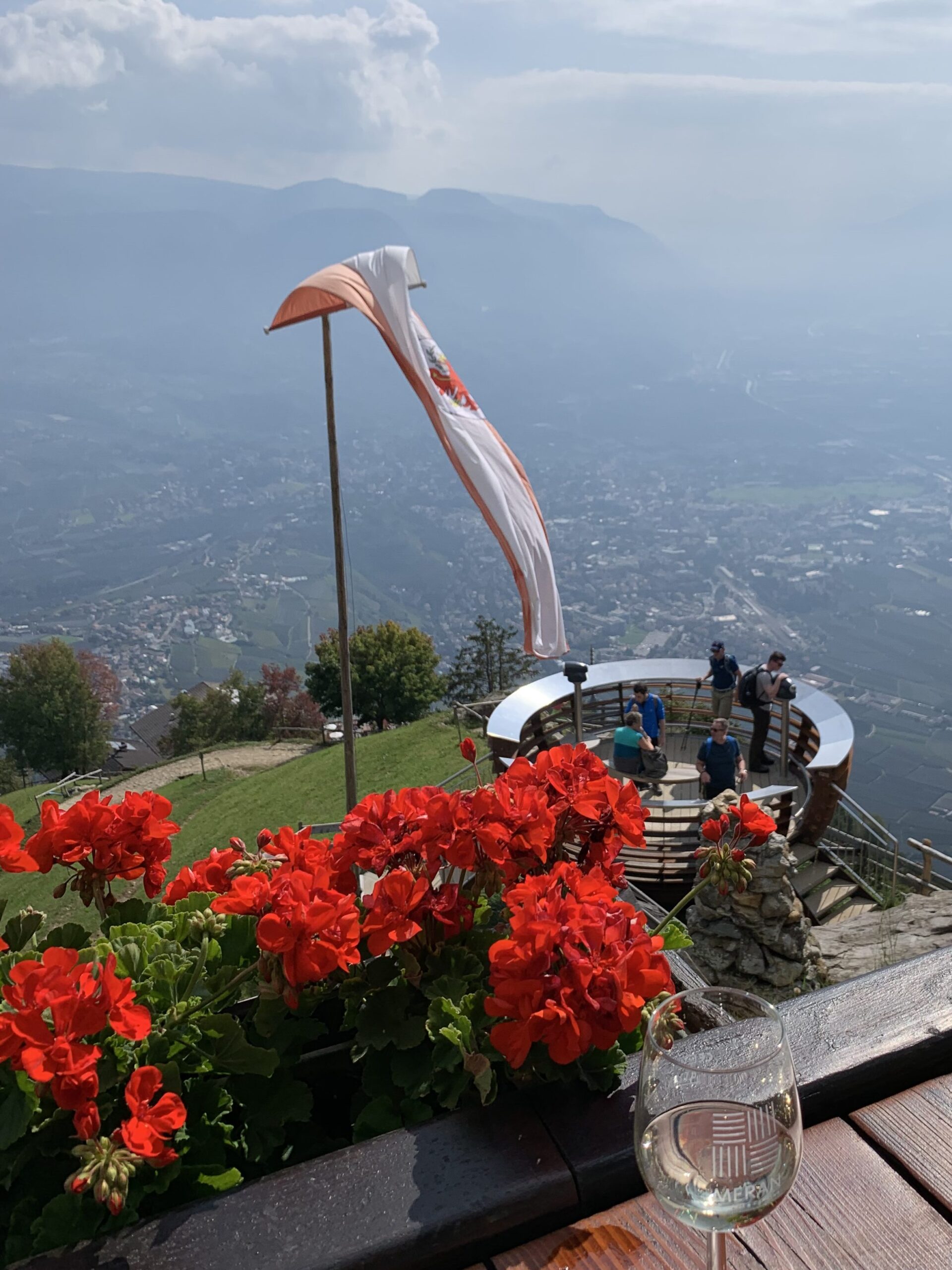 A sweeping view from a balcony takes in red geraniums and a mountain valley in northern Italy at Gasthaus Steinegg.