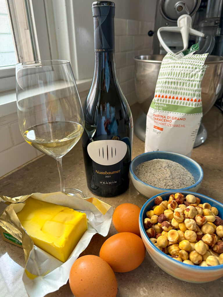 Baking ingredients are set out on a counter below a bright window. A bottle of wine and wine glass are centered.