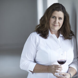 Sue Tolson standing in front of window in white shirt holding glass of Hungarian wine