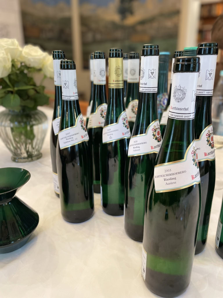 An array of Karthäuserhof bottles stand on a table along with a vase of white flowers.