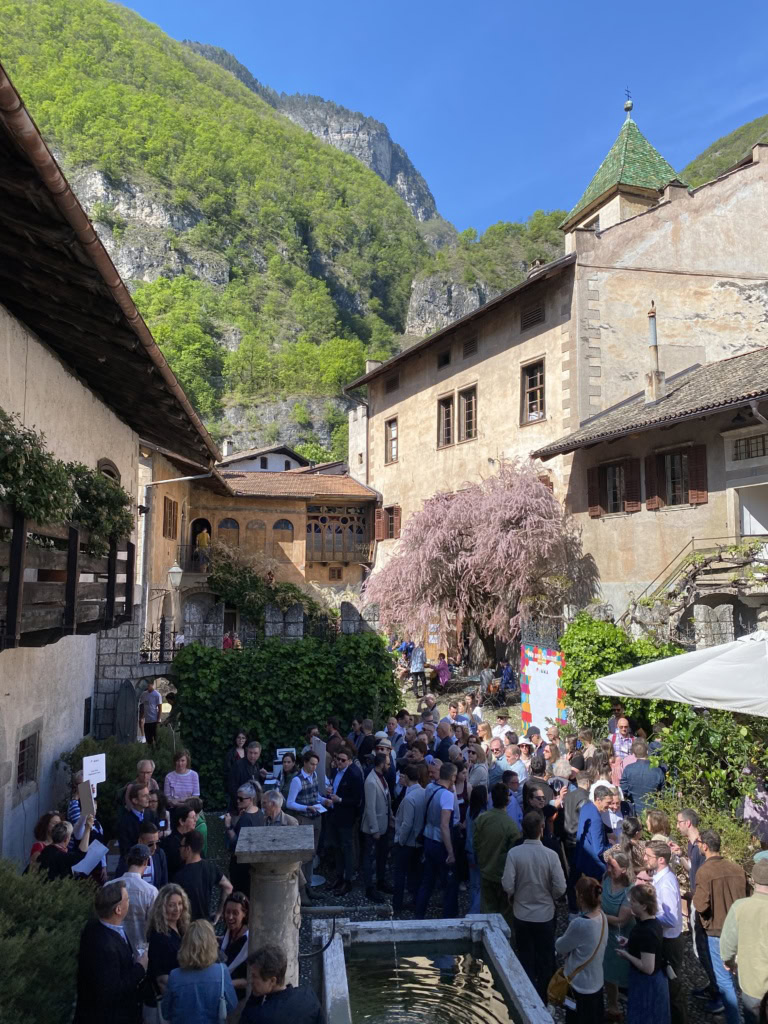 At the Summa wine fair a small crowd gathers in the shadows of ancient buildings and Alpine peaks under blue skies.