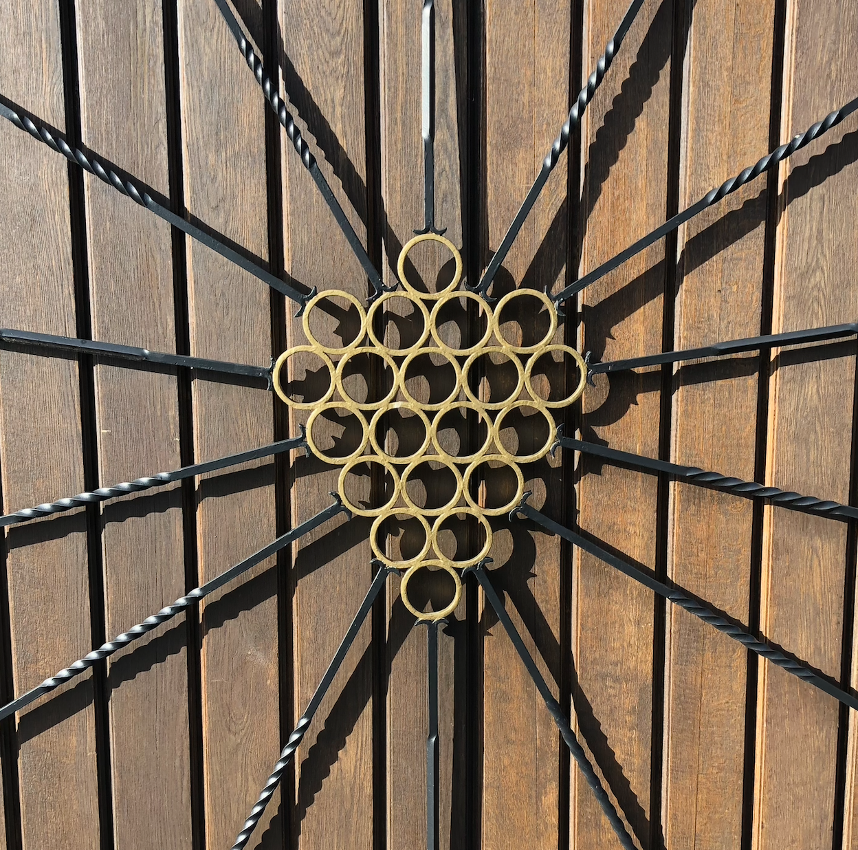 A decorate metal door grill features a bronze grape cluster with black metal rays emenating from it.