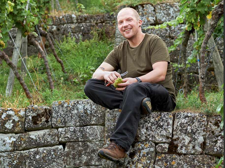 Moritz Haidle sits on a stone wall in his vineyard