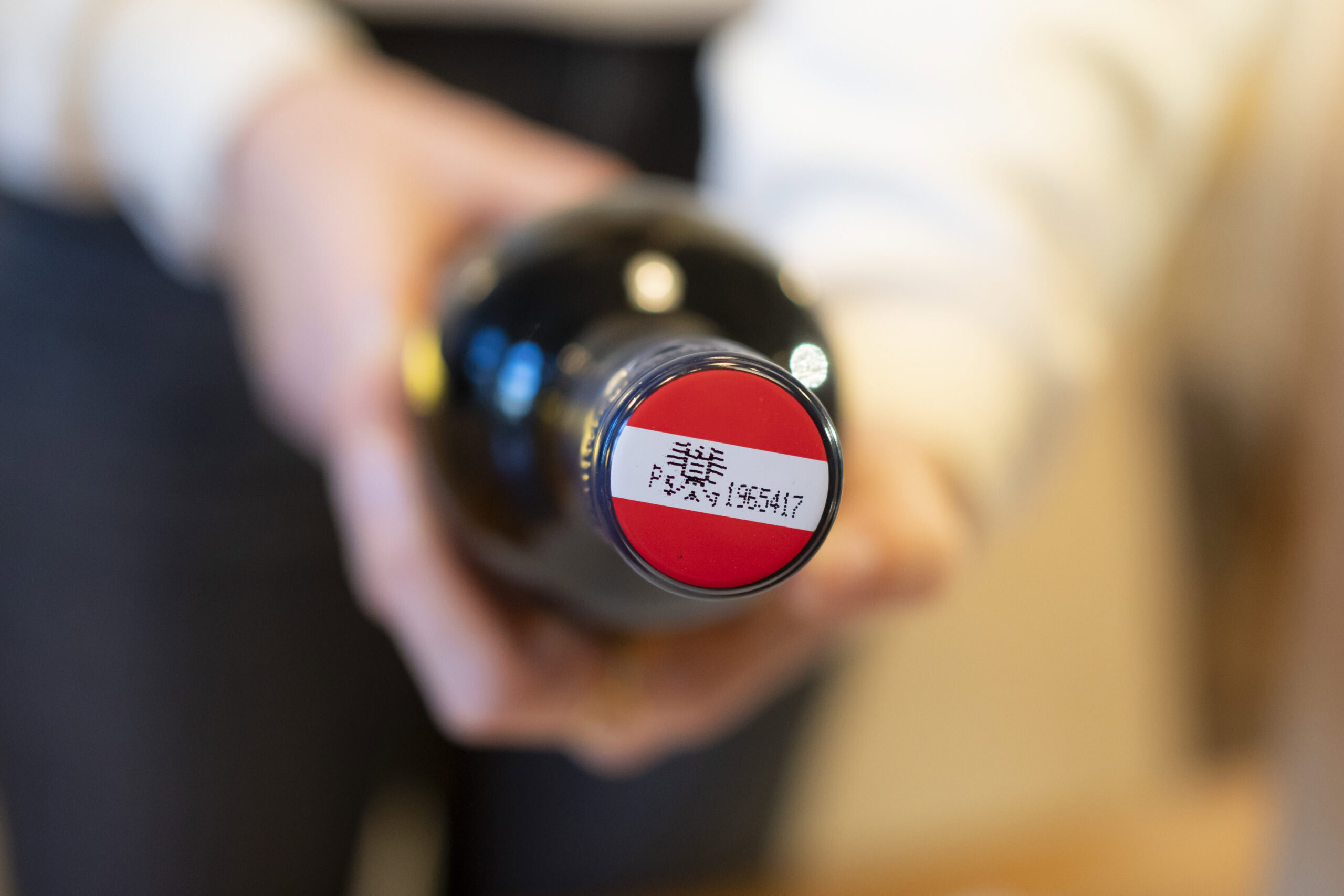 A bottle of wine with the red-white-red Austrian wine banderole is pointed at the viewer.