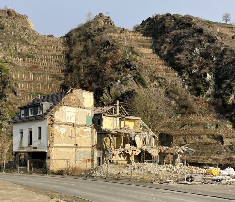 A small building half destroyed by flood is in the foreground, in the background a terraced vineyard.