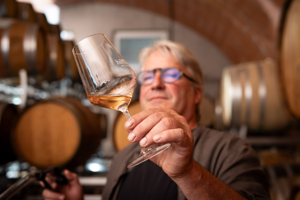 Matthias Höfflin examines a glass of wine in a barrel room