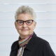 Ruth Landy, writer, dressed in black jacket with striped scarf and glasses