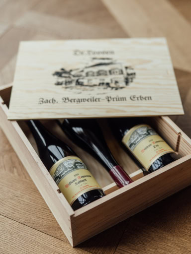 An open wooden wine crate stamped with Zach. Bergweiler-Prüm Erben containing three bottles of Loosen old vines Riesling.