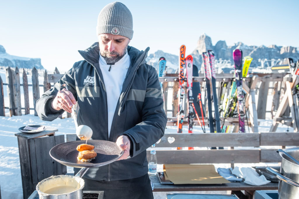 Chef plating a dish at a mountain hut during the Gourmet Skisafari Alta Badia, Dolomites in the background