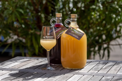 Two jugs of wine, one red, one orange and cloudy sit near a glass filled with the orange cloudy liquid.